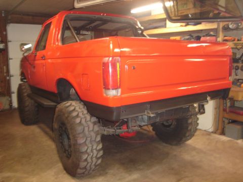 1989 Ford Bronco - This orange SUV is modified with large tires and appears to be undergoing some work in a garage.