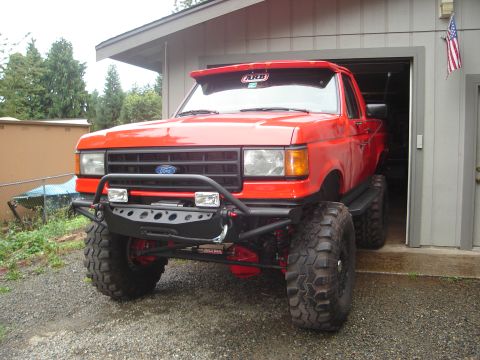 1989 Ford Bronco - This modified Ford Bronco, likely from the late 1980s, sits outside a garage with an American flag visible.