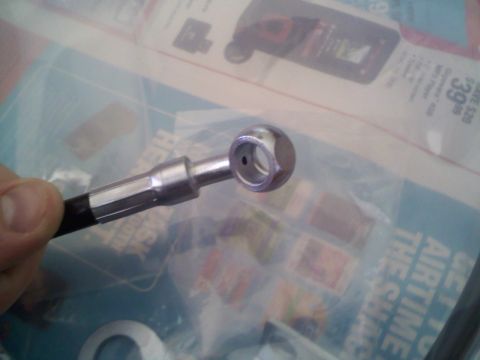 1994 Ford Bronco - A close-up view of a brake line fitting, likely for a vehicle, is held by a hand against a background of what appears to be a catalog or ad…