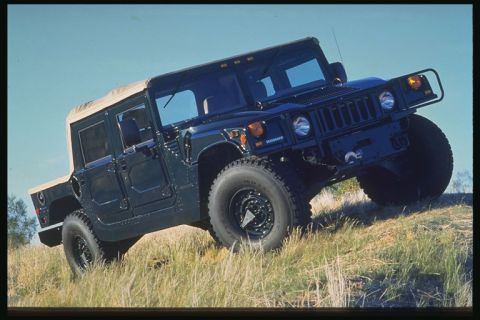 1998 Ford Crown Victoria - A dark green Hummer H1 with a tan soft top drives up a grassy hill under a clear blue sky.