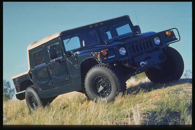 Dark green Hummer H1 with tan soft top on grassy incline