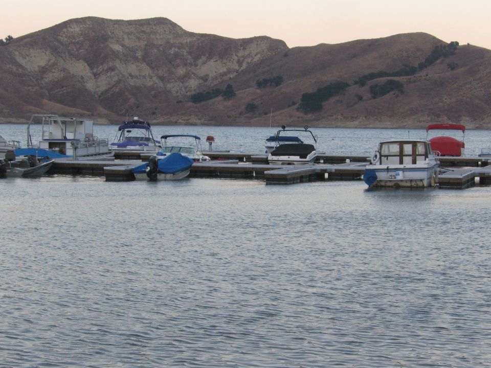 Several boats are docked on a pier with a large hill in the background