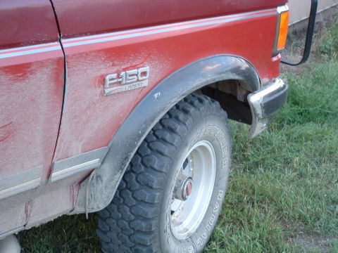 1988 Ford F-150 - A dusty red Ford F-150 is viewed from the side, highlighting its fender and tire.