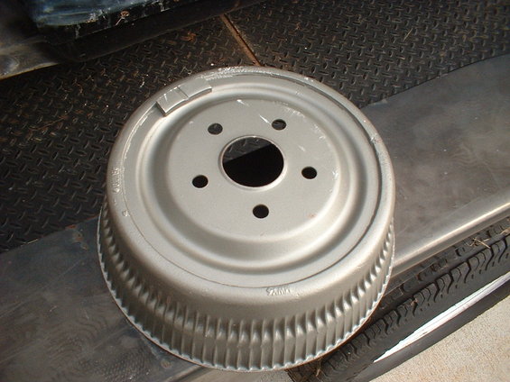Silver brake drum with five bolt holes and ribbed outer edge. It sits on a tire