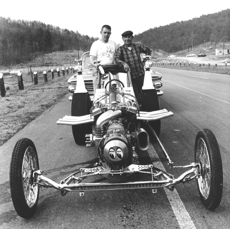 Black-and-white photo of two men with a vintage front-engine dragster