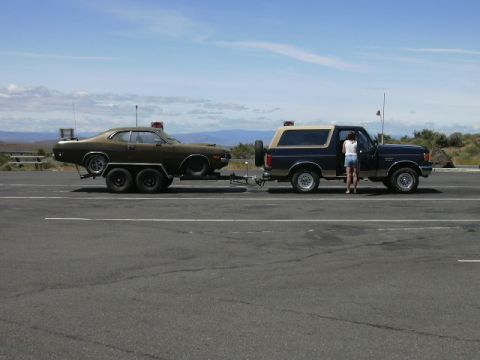 1991 Ford Bronco - A 1991 Ford Bronco is seen from the side, towing a brown muscle car on a trailer.