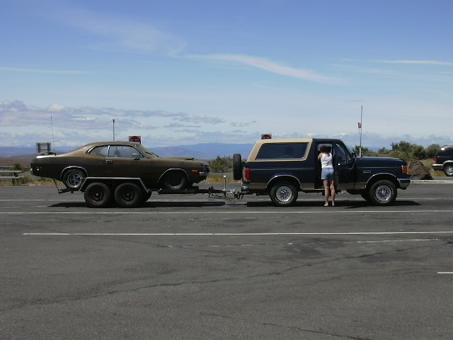 Ford Bronco towing a brown classic car on a trailer
