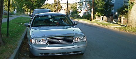 2000 Ford Crown Victoria - A silver sedan is parked on the side of a residential street, with another vehicle behind it.