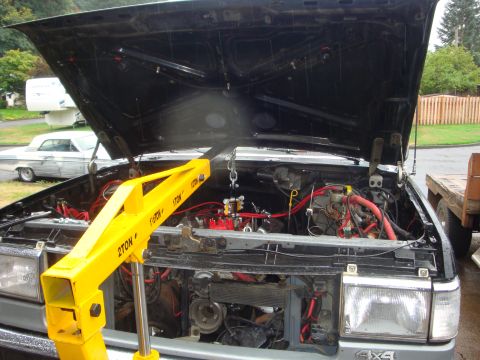 1989 Ford Bronco - Engine bay of a vehicle with the hood open, a yellow engine hoist is positioned over the engine.
