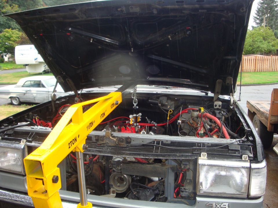 Yellow engine hoist chained over the open engine bay of a silver Ford 4x4 truck