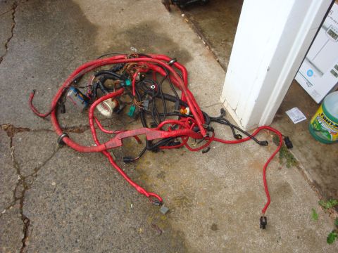 1989 Ford Bronco - A tangled automotive wiring harness lies on a cracked concrete surface next to a white pillar and a green bottle.