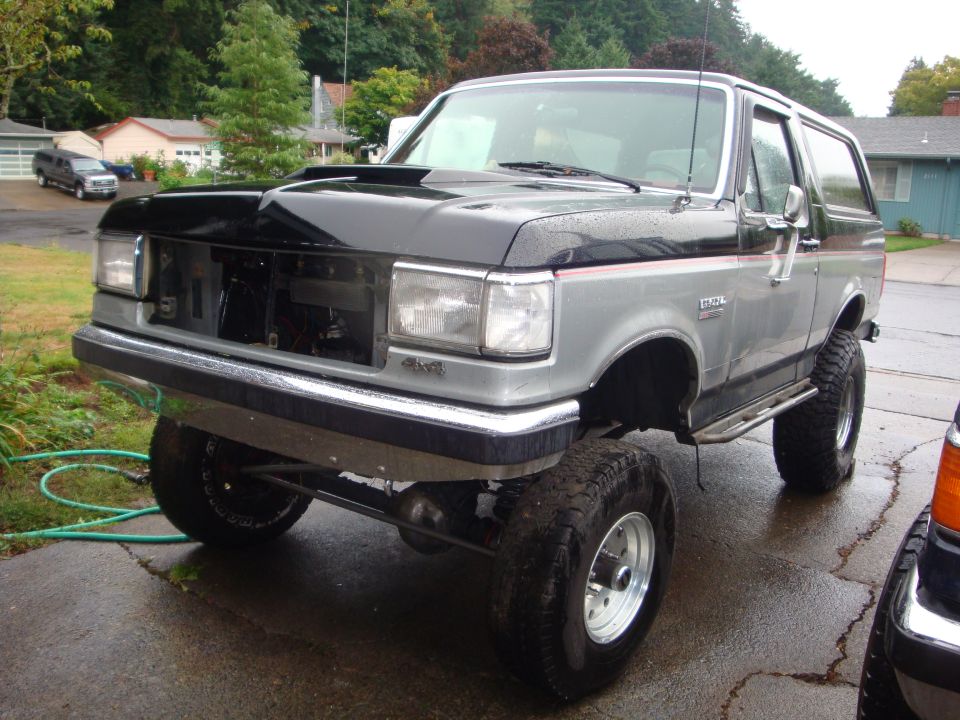 Lifted silver Ford Bronco on wet driveway with grille removed, radiator exposed