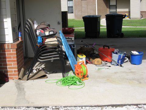 1986 Ford Bronco - Outdoor items and stacked chairs are stored on a concrete patio next to a building.