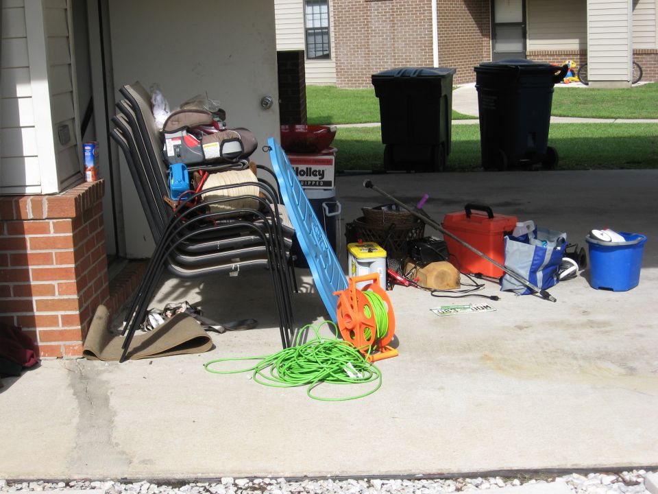 Stack of chairs, extension cord reel, tools, and buckets on a concrete patio