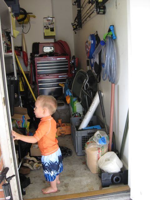 1986 Ford Bronco - A young child stands in the entrance of a messy garage filled with tools, fishing gear, and various stored items.