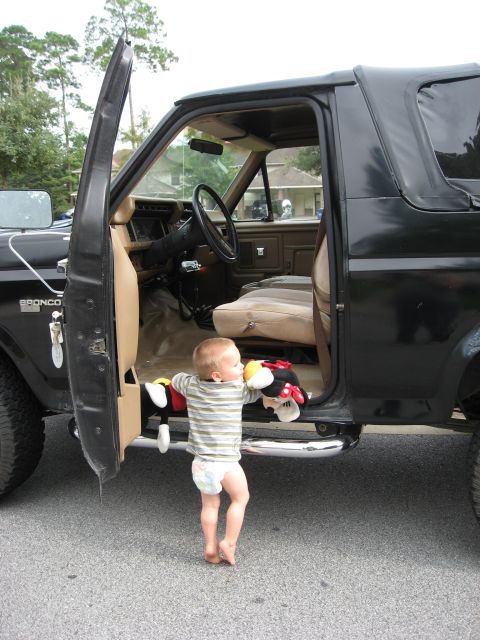 1986 Ford Bronco - A toddler reaches for the interior of a 1986 Ford Bronco, holding Mickey Mouse plush toys.
