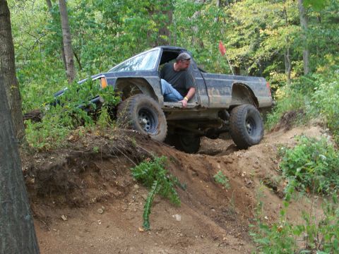 1989 Ford Bronco - A man navigates a black off-road truck through a challenging dirt trail surrounded by trees.