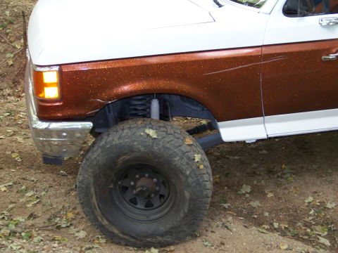 1989 Ford Bronco - The front quarter panel and large tire of a 1989 Ford Bronco are visible in this close-up shot.