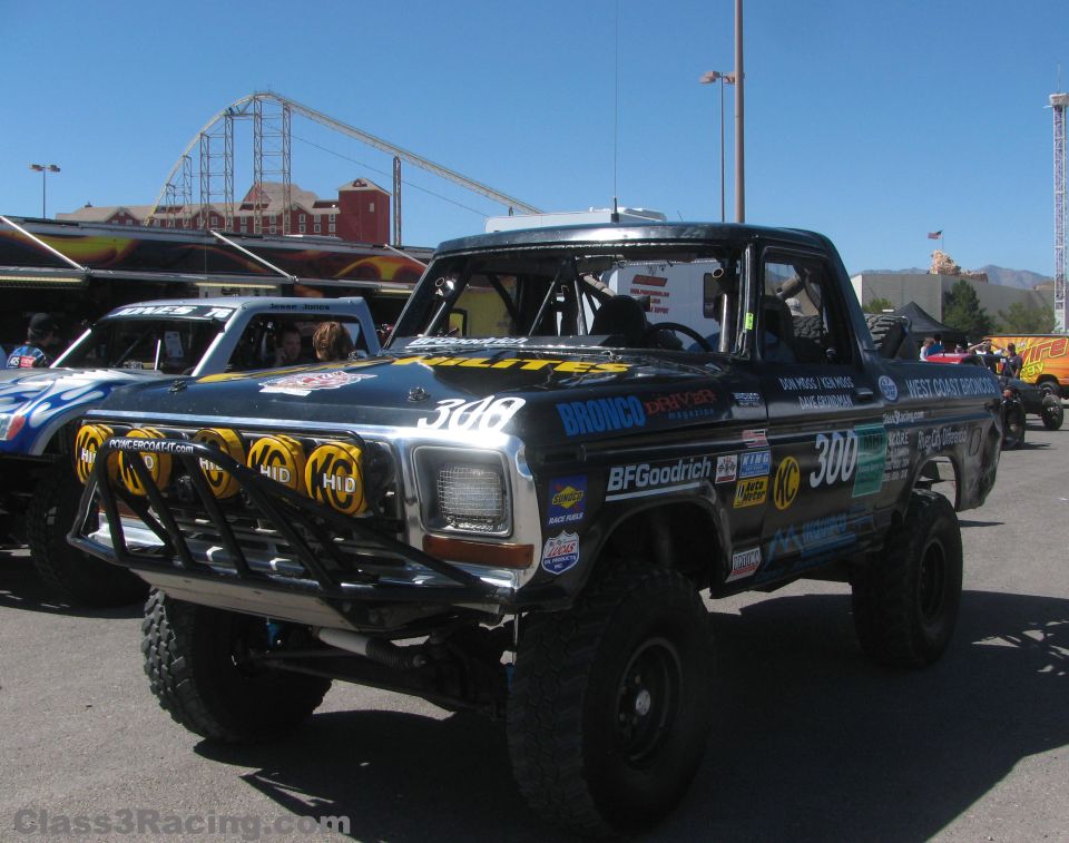 Black number 300 off-road Ford truck in a pit area with amusement park in background