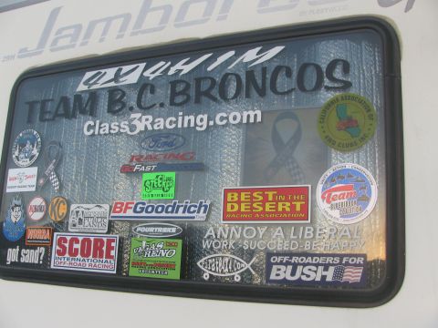 1990 Ford Bronco - trailer window plastered with racing and sponsor stickers, including Team B.C. Broncos, Class3Racing.com and BFGoodrich.