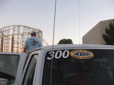 1990 Ford Bronco - Close view of a number 300 NORRA decal on a white truck's rear window with a man and roller coaster in the background.