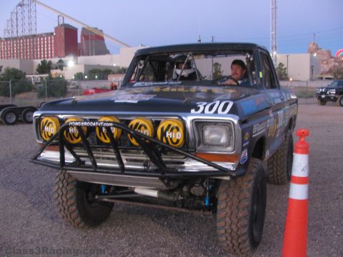 1990 Ford Bronco - black number 300 off-road Ford race truck with a row of yellow HID lights staged at dusk beside a traffic cone.