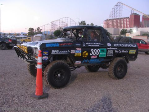 1990 Ford Bronco - Front three-quarter view of a black number 300 West Coast Broncos race truck staged by an orange cone at dusk.