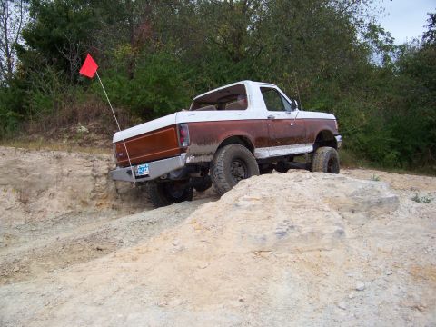 1989 Ford Bronco - A lifted Ford Bronco navigates a challenging off-road terrain with a red flag attached to its antenna.