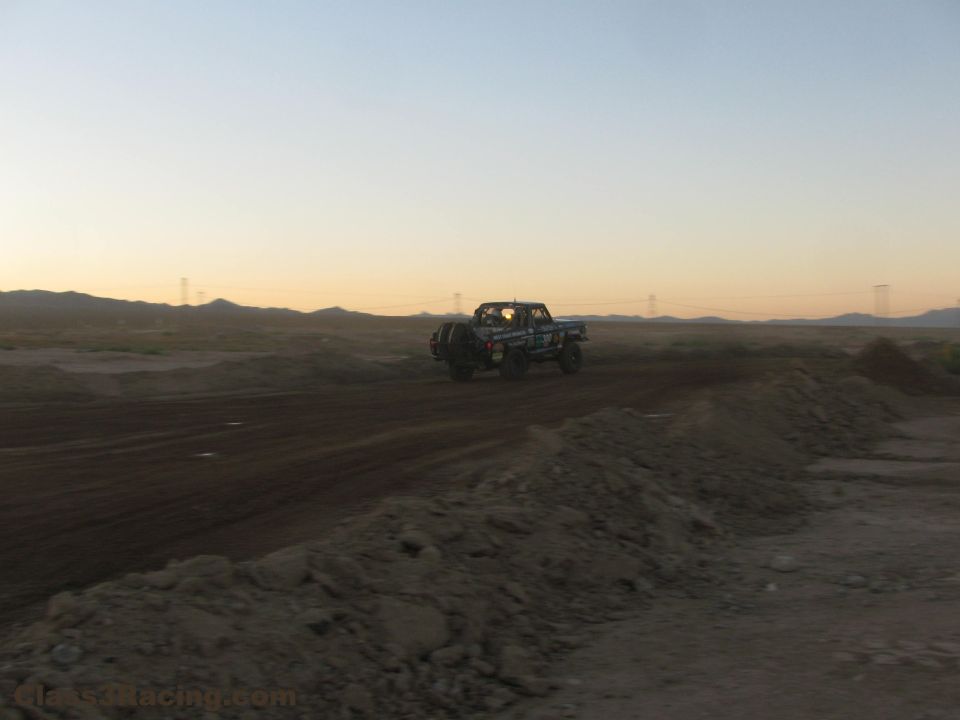Off-road race truck on a desert dirt road at dusk seen from behind