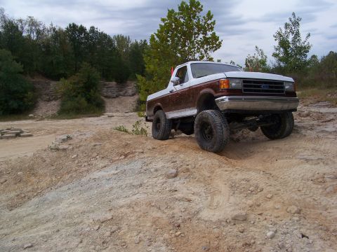 1989 Ford Bronco - A lifted Ford F-Series truck navigates a rocky, off-road terrain under a cloudy sky.