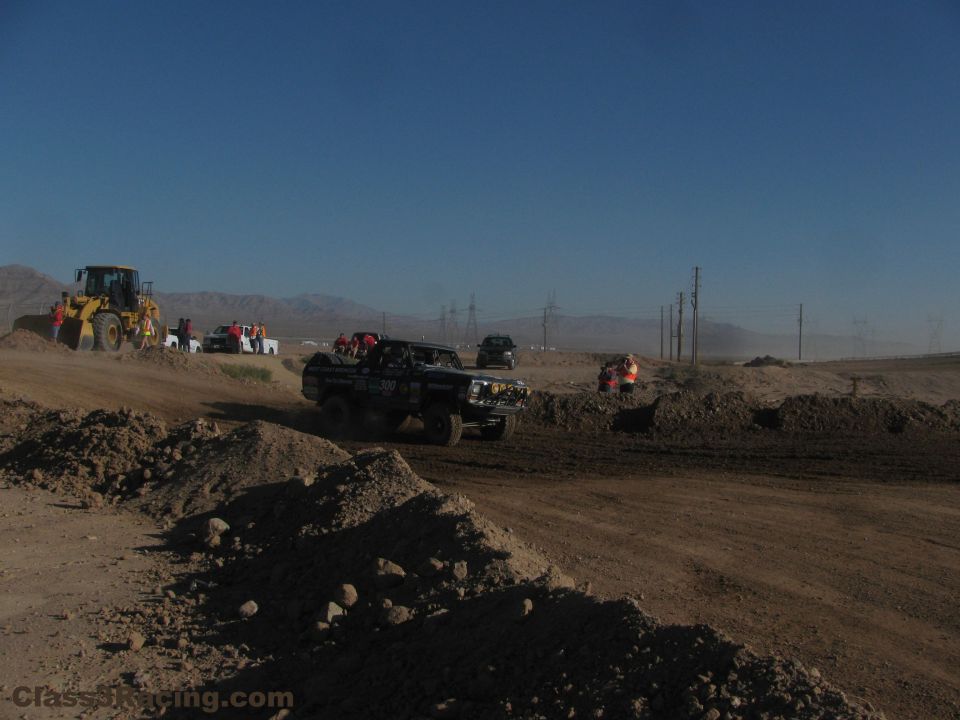 Off-road race truck on a desert dirt course with crews and loader