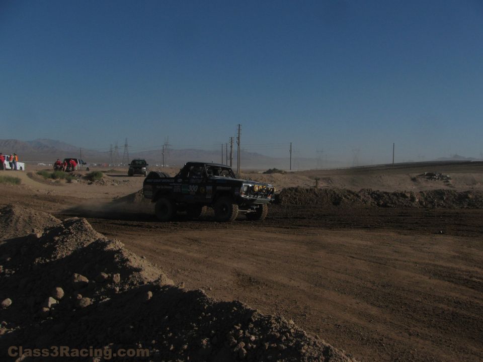 Off-road race truck rounding a dirt berm on a desert course