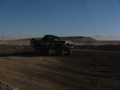 1990 Ford Bronco - number 300 West Coast Broncos race truck travels a dusty desert dirt course with hazy hills under a deep blue sky.