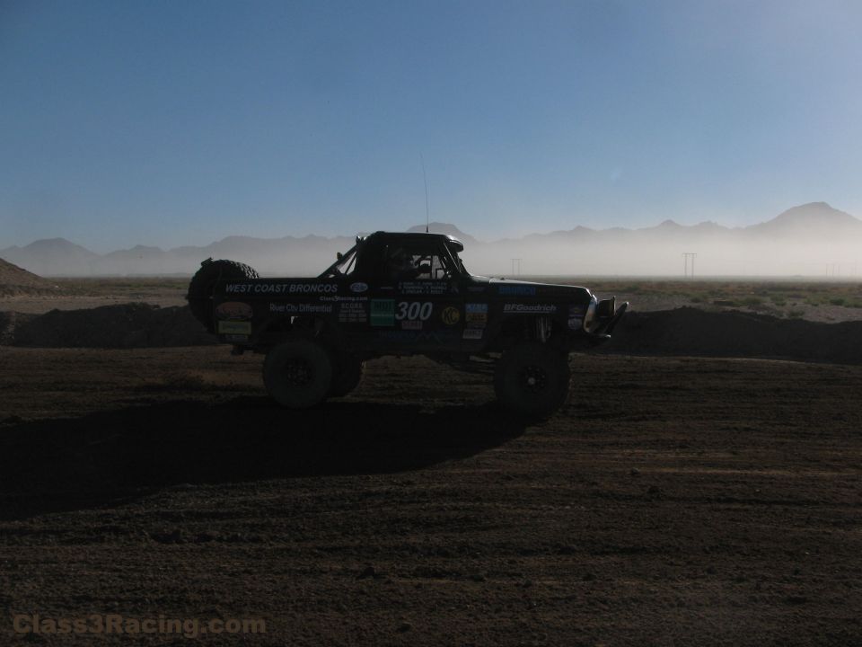 Number 300 off-road race truck silhouetted in desert dust haze