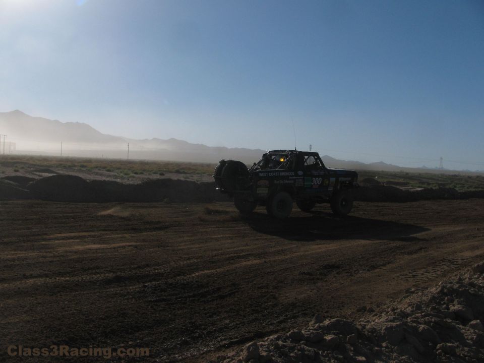 Silhouetted off-road race truck on a dusty desert race course at sunrise