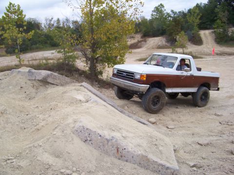 1989 Ford Bronco - A two-tone Ford Bronco navigates a challenging off-road terrain with concrete obstacles.