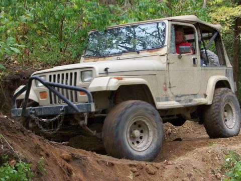 1989 Ford Bronco - A tan Jeep Wrangler navigates a steep dirt incline during an off-road excursion.