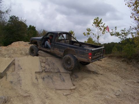 1989 Ford Bronco - Jeep Comanche pickup truck with roll cage climbing a dirt hill during an off-road event.
