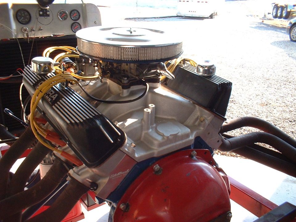 Close-up of a V8 engine with chrome air cleaner, aluminum intake, and black valve covers. Headers are visible