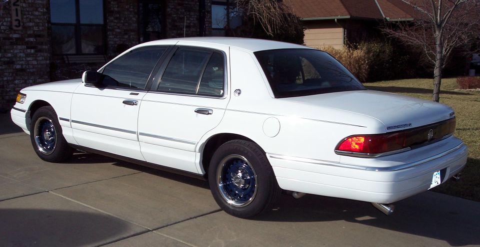 White sedan parked in a driveway. It has chrome trim and blue rims