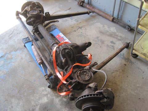 1979 Ford Bronco - A disassembled front axle assembly and driveshaft, showing signs of rust and wear, are placed on a blue dolly.