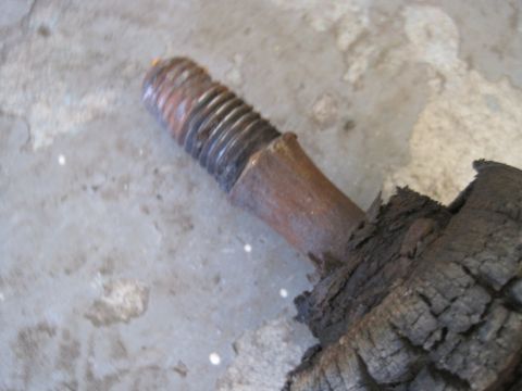 1979 Ford Bronco - Close-up of a rusted bolt attached to charred wood on a concrete surface.