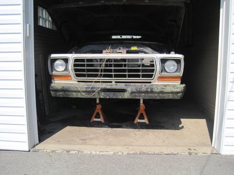 1979 Ford Bronco - This truck's front end is raised on jack stands inside a garage, with its hood open.