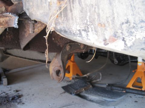1979 Ford Bronco - Close-up of a heavily rusted suspension part, supported by orange jack stands, indicating repair or maintenance work.