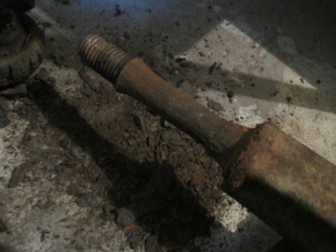 1979 Ford Bronco - Close-up of a rusted metal part with threads and a hexagonal end lying on a concrete surface.