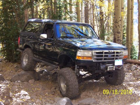 1994 Ford Bronco - This 1994 Ford Bronco navigates a challenging, rocky trail surrounded by trees.