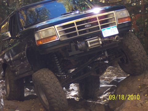 1994 Ford Bronco - This lifted Ford Bronco is navigating a rocky trail, showing off its off-road capabilities.
