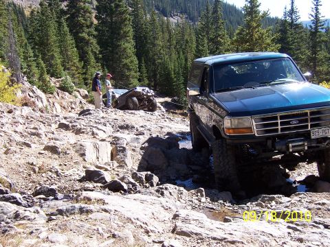 1994 Ford Bronco - A blue Ford Bronco navigates a rocky trail, with another vehicle stuck in the background.