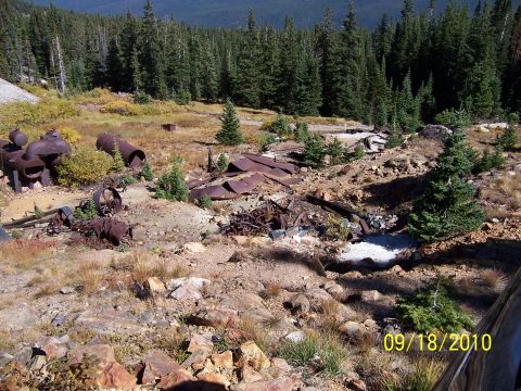 1994 Ford Bronco - An abandoned mine site with rusted metal debris and scattered rocks under a forest canopy.