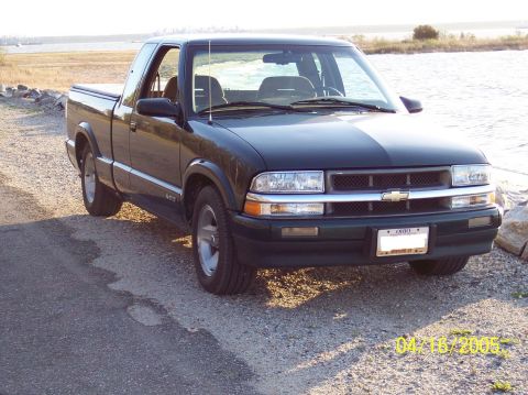 1986 Ford Bronco - A dark green pickup truck is parked on a gravel surface next to a body of water.